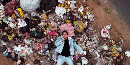 Un homme allongé sur un tas de déchets faisant un signe à la main sur sa bouche de se taire