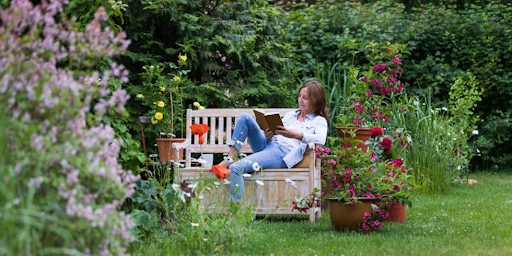 Une femme assise sur une chaise dans son jardin en train de lire un livre