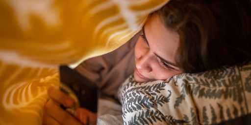 Une jeune femme dans son lit jouant à son téléphone